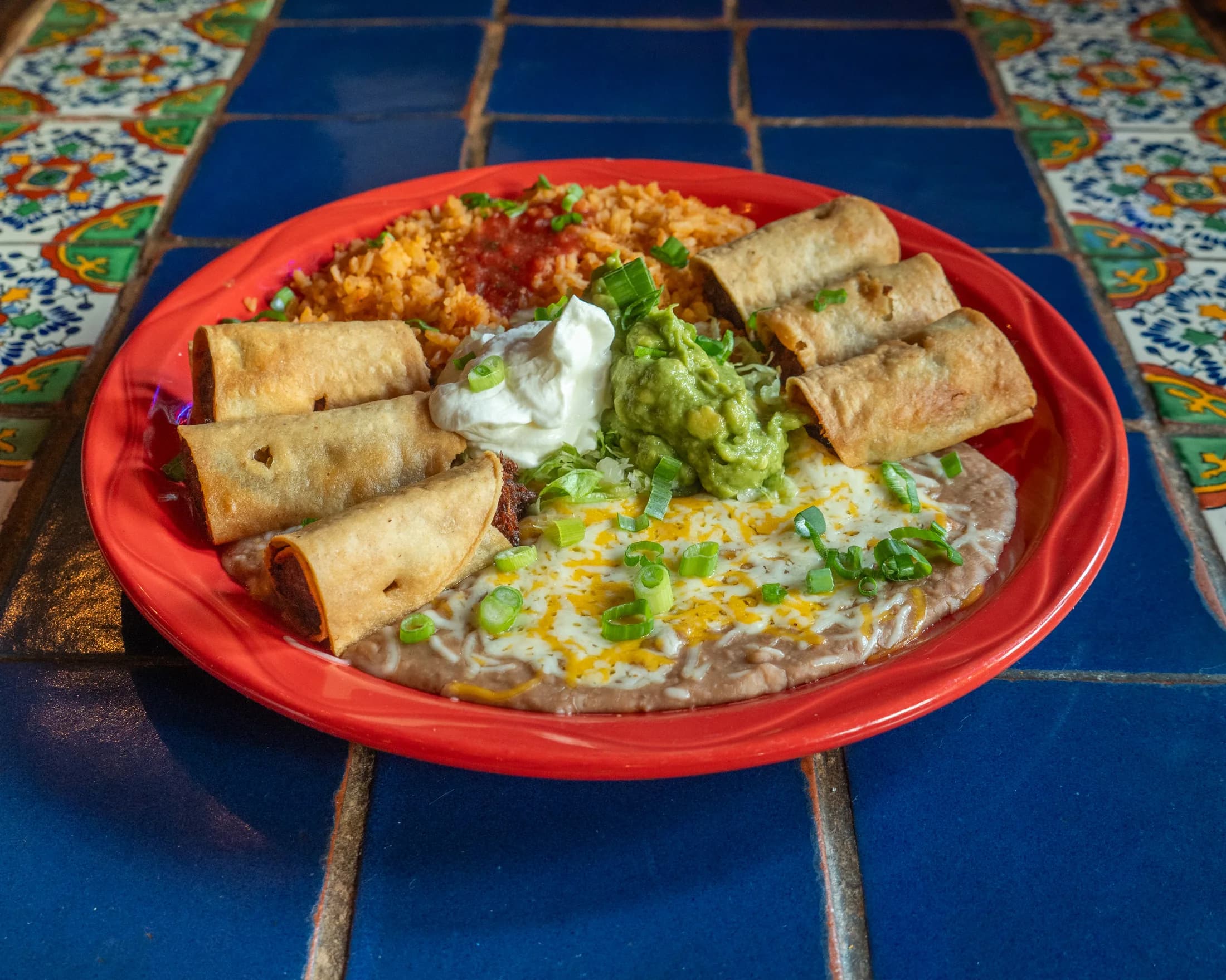 A taquito combination served with rice, beans, guacamole, and sour cream